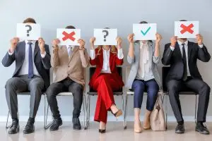 Young people holding paper sheets with different marks while sitting on chairs indoors